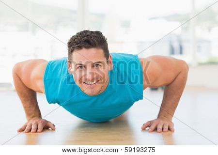 Portrait of a smiling young man doing push ups in the bright gym