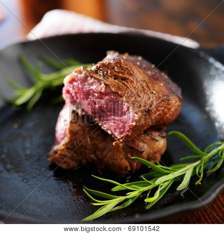 rare steak cut in half on iron skillet with rosemary