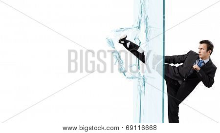 Young determined businessman breaking glass with karate kick