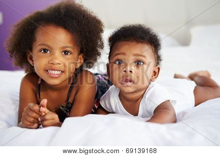 Sister With Baby Brother Lying On Parent's Bed