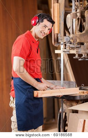 Portrait of young carpenter marking on wood with pencil by bandsaw in workshop