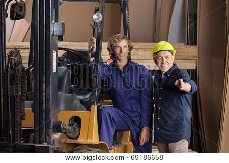 Male carpenters looking away while standing by forktruck in workshop