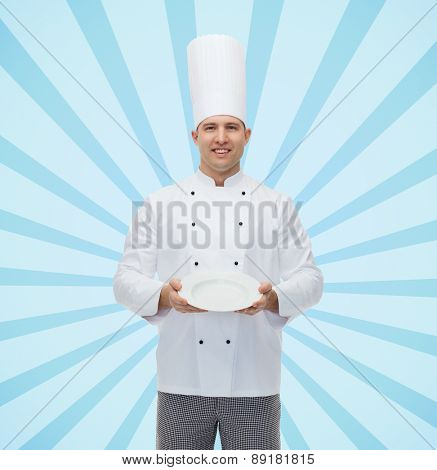cooking, profession, advertisement and people concept - happy male chef cook showing something on empty plate over blue burst rays background