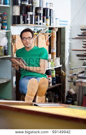Portrait of relaxed worker using digital tablet while sitting in paper factory