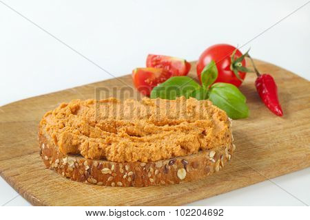 slice of bread with spicy meat spread served together with chili pepper and fresh tomatoes, on the wooden cutting board