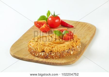 wooden cutting board with slice of bread and spice meat spread together with fresh cherry tomatoes and chili pepper
