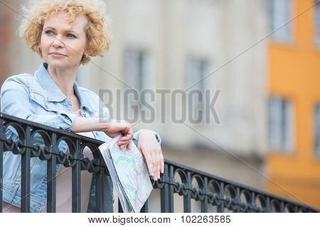 Thoughtful middle-aged woman holding map while leaning on railing