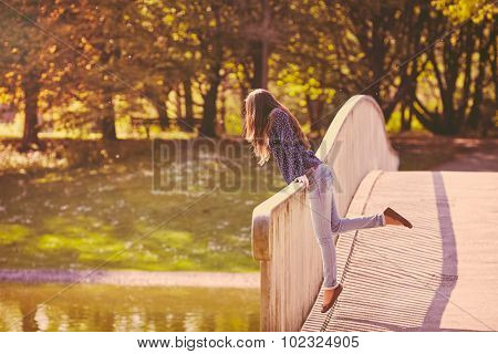 Retro colored full length portrait of young long-haired woman wearing blue shirt and jeans leaning on railing in summer park - lifestyle concept