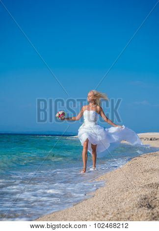 Young bride in wedding drees having fun on the beach in Greece