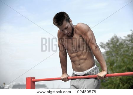 fitness, sport, training and lifestyle concept - young man exercising on horizontal bar outdoors