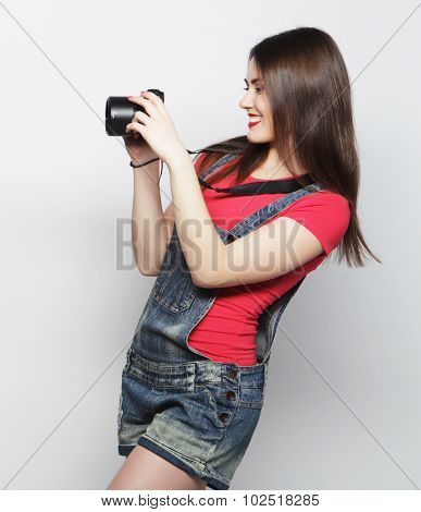 Beautiful young woman with camera over gray background