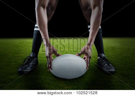 Low section of sportsman holding ball while playing rugby against green field