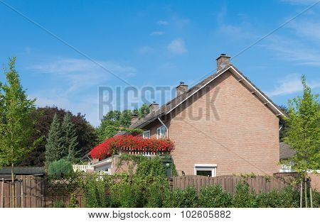 simple house with large balcony full with blooming red geranium flowers