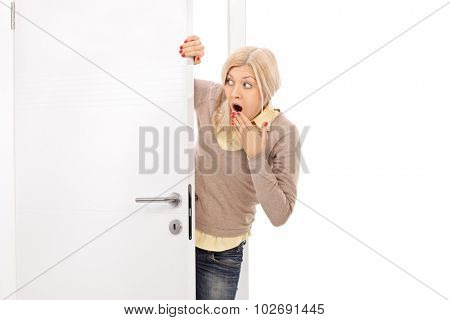 Blond woman peeking from behind a door and making shocked grimace isolated on white background