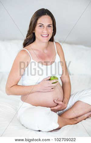 Portrait of pregnant woman sitting with Granny Smith apple on bed