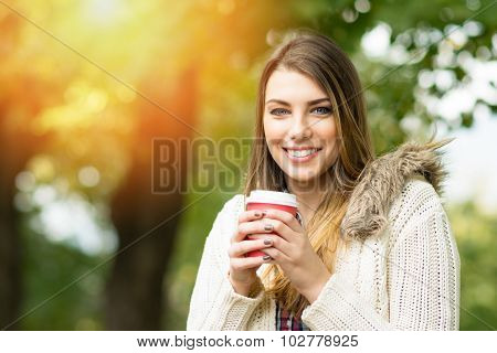 Young woman with takeaway coffee in park in autumn