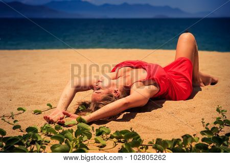 Upper View Blond Girl In Red Frock Lies On Sand Bends Knee