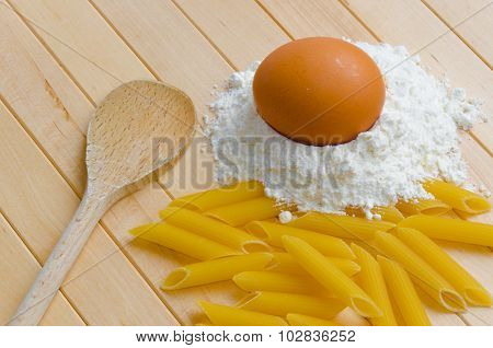 Egg on flour with pasta and wooden spoon on wooden background