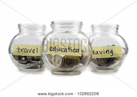 Coins In Glass Container With Travel, Saving And Education Label On White Background. Selective Focu