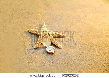 Compass with sea star on sand beach background