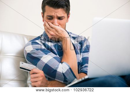 Upset man holding credit card at home