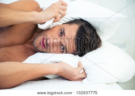 Portrait of a handsome man lying on the bed with pillow on head at home