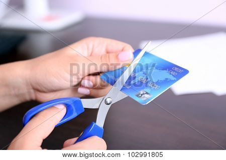 Woman's hands cutting bank card with scissors on wooden table background