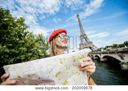 Young and happy woman tourist sitting with paper map in front of the Eiffel tower in Paris
