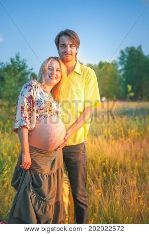 A pregnant beautiful woman with her husband on the river bank beach smiling and touching her mehandi ornament belly with love and care. Happy couple, family relax on sunset