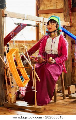 Inle Lake Myanmar - January 04 2007: Young woman of Kayan Lahwi (Padaung) people wearing brass coils on long neck weaving traditional Burmese handmade textile in village on Inle lake in Shan state.
