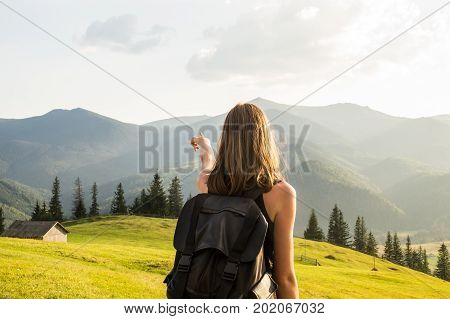 Female hiker points to a destination of trip in mountains. Young girl stands at hillside of ukrainian carpathian mountains and looks at distant mountain peaks