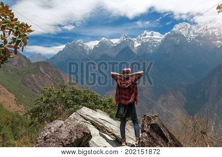 Traveler has reached the summit of mountain. Young woman is relaxing and enjoying beautiful view of mountains in Shangri-La