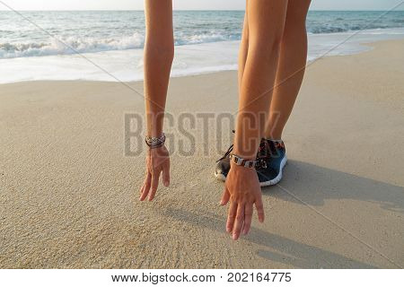 Close up of female is standing in forward bend on the beach hands to feet
