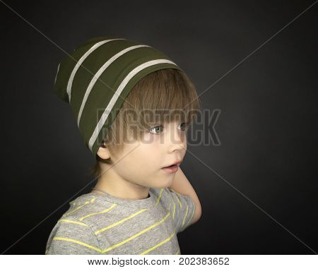 Portrait of a stylish three-year-old child in a striped hat on a dark grey background
