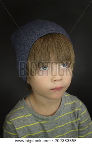 Portrait of a stylish three-year-old child in a grey hat on a dark grey background
