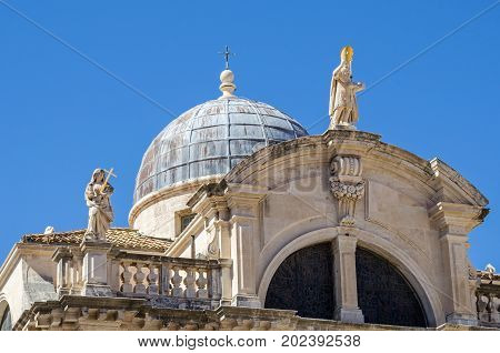 Top of the facade of the baroque Church of St. Blaise in the old city of Dubrovnik with the Statue of Saint Blaise the patron of the city and a personifications of Faith to the left on the balustrade. The saint shows in his left hand a scale model of the