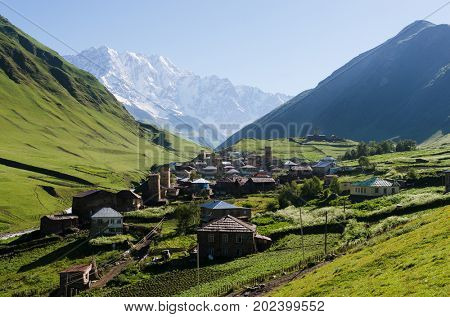 Summer mountain landscape with a snowy peak and a green valley. Old village with stone houses and medieval towers. Ushguli community. View of Shkhara Mount. Main Caucasian ridge, Zemo Svaneti, Georgia