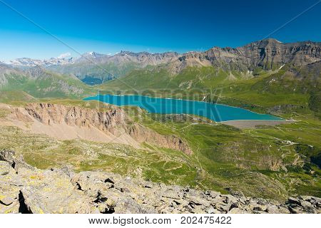 High Altitude Blue Lake, Dam On The Italian French Alps. Expansive View From Above, Clear Blue Sky.
