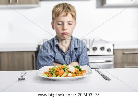lovely boy showing boring expression with fresh colorful vegetables