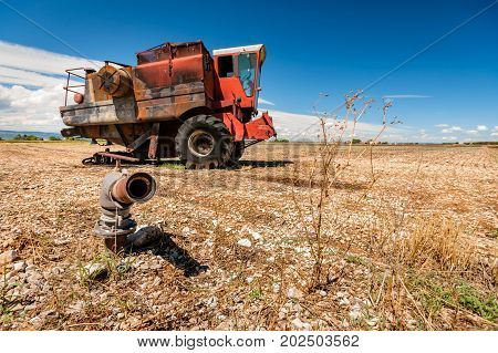 Old burned agriculture combines in a flattened grainfield under a blue sky with white clouds in the countryside of france