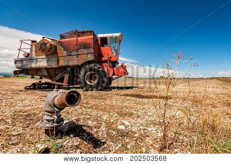 Old burned agriculture combines in a flattened grainfield under a blue sky with white clouds in the countryside of france