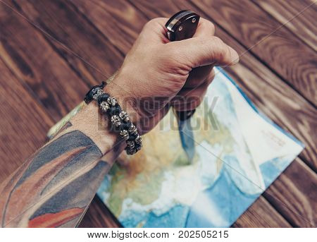 Unrecognizable man holding jackknife and pointing to map on a wooden background view of hand.