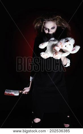 Horror shot: evil demonic girl with torn rabbit toy and bloody knife in hands