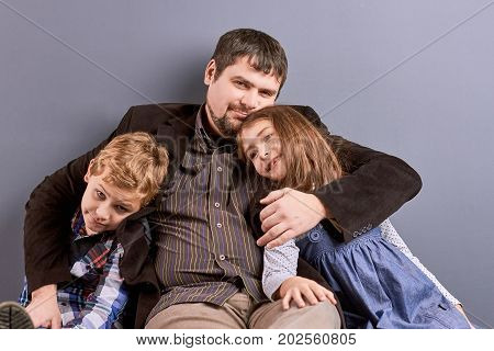 Father hugging his son and daughter. Studio shot of caring father sitting with two kids. Happy father and joyful kids. Concept of family happiness.