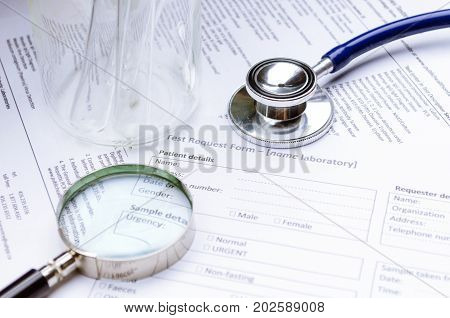 stethoscope magnifying glass test tube beaker and patient information form on desk healthcare technology medical report record and history patient concept selective focus