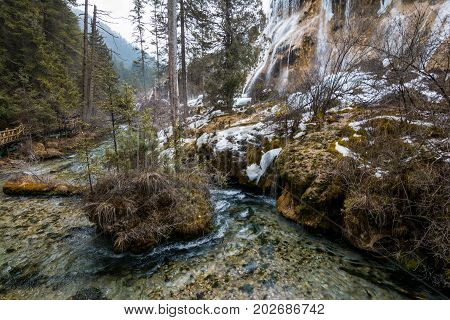 Waterfall in the forest. Stream of water on the rocks. Clean and cold water over the coniferous forest. Stones in the snow. Powerful rocks and a stream of water