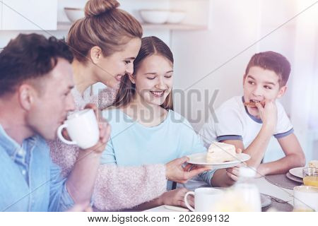 Family meal tradition. Selective focus on a thoughtful mother taking care of her family and treating children with a cake while all sitting at a kitchen island and chatting during a family breakfast.