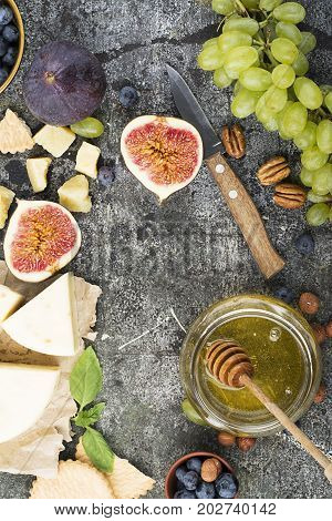 Cheese board for snacks, tricks, meetings with friends, on a gray stone background: assorted cheeses, young cheese, parmesan, cheese with fenugreek, figs, nuts, honey, grapes Top View