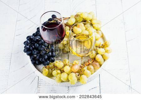Red and white wine in glasses with grapes on white background. Assortment of autumn harvest beverages. Copy space