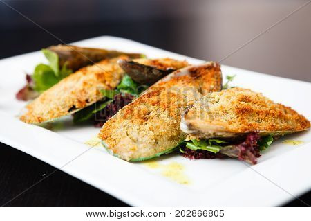 Seafood. Shellfish mussels. Baked mussels with cheese, parsley and lemon in shells served on a stone board.